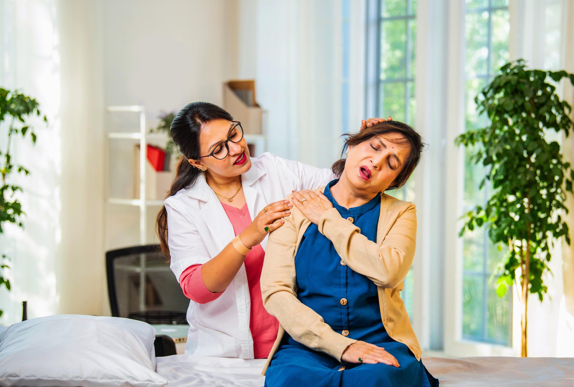 Donna con dolore cervicale che riceve un trattamento da un’operatrice sanitaria in studio. Terapia per alleviare la tensione muscolare e i sintomi del dolore al collo.
