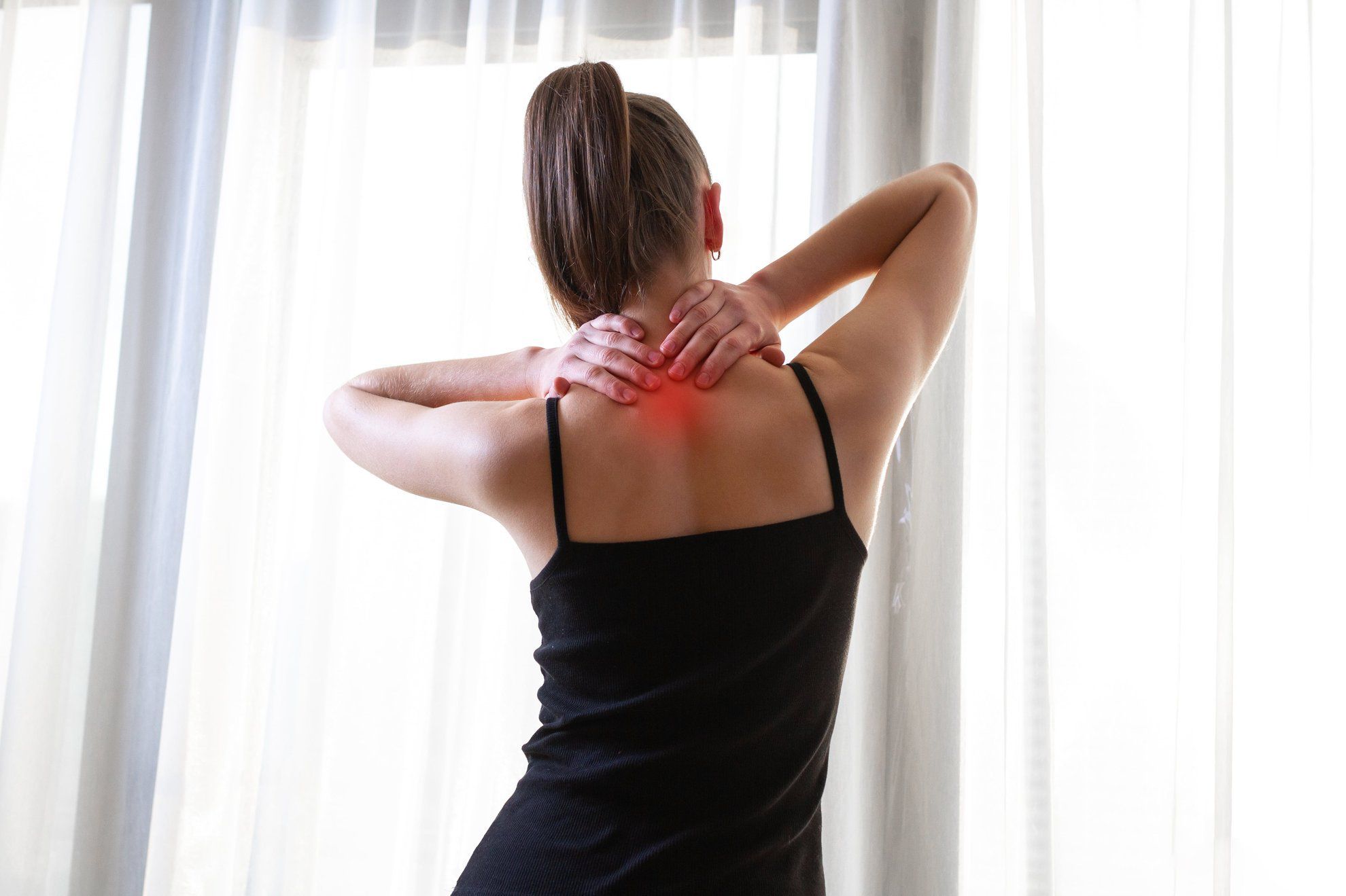 Giovane donna che si massaggia il collo perché soffre di dolore alla schiena alta, stirando i muscoli.